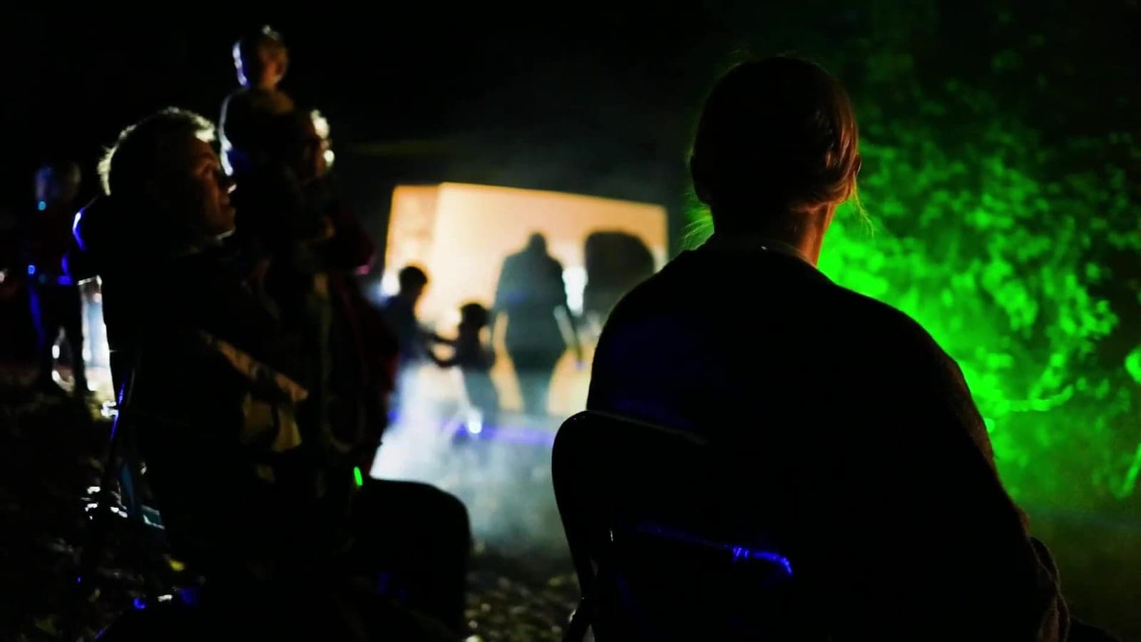 An audience watching a lit screen in green-lit woodland at Vogrie Pogrie